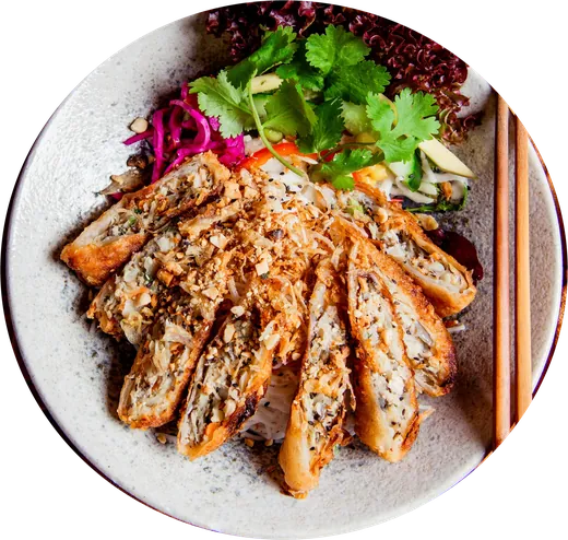Reisnudeln mit aufgeschnittenen Frühlingsrollen, Kräutern und Salat auf einem hellen Teller, von oben
