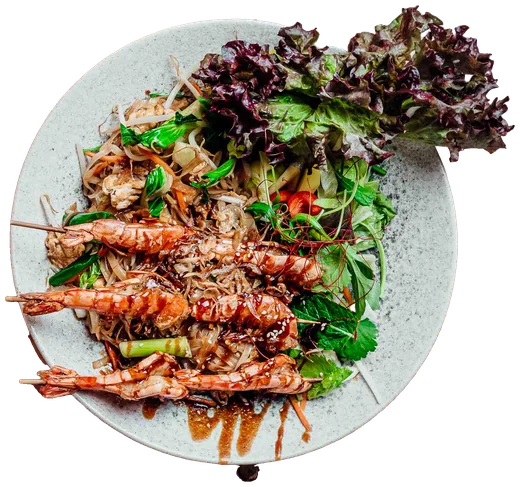 Gebratene Reisbandnudeln mit Garnelenspießen und Salat auf einem hellen Teller, von oben