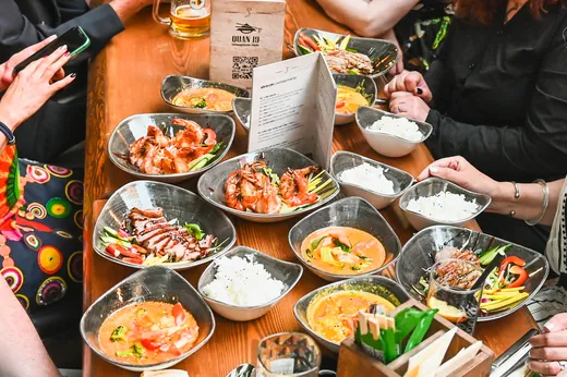 Ein langer Tisch voller Schalen mit Curry, Reis und Gegrilltem, Hände greifen zu