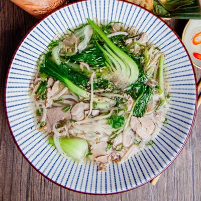 Phở bò mit Rindfleisch und Pak Choi in einer blau gestreiften Schale
