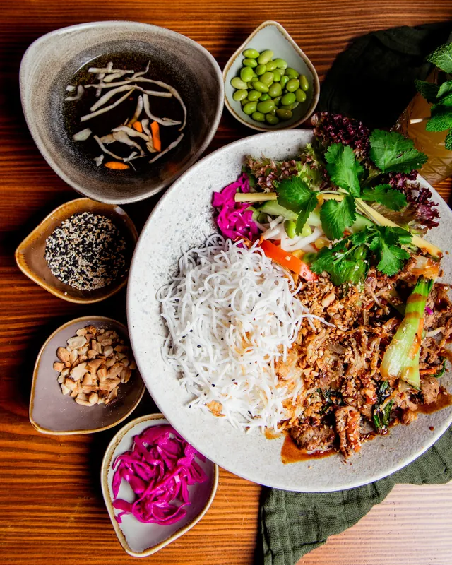 Bun Bowl mit gegrilltem Rindfleisch, Reisnudeln, Kräutern und kleinen Schalen mit Erdnüssen, Sesam und Edamame